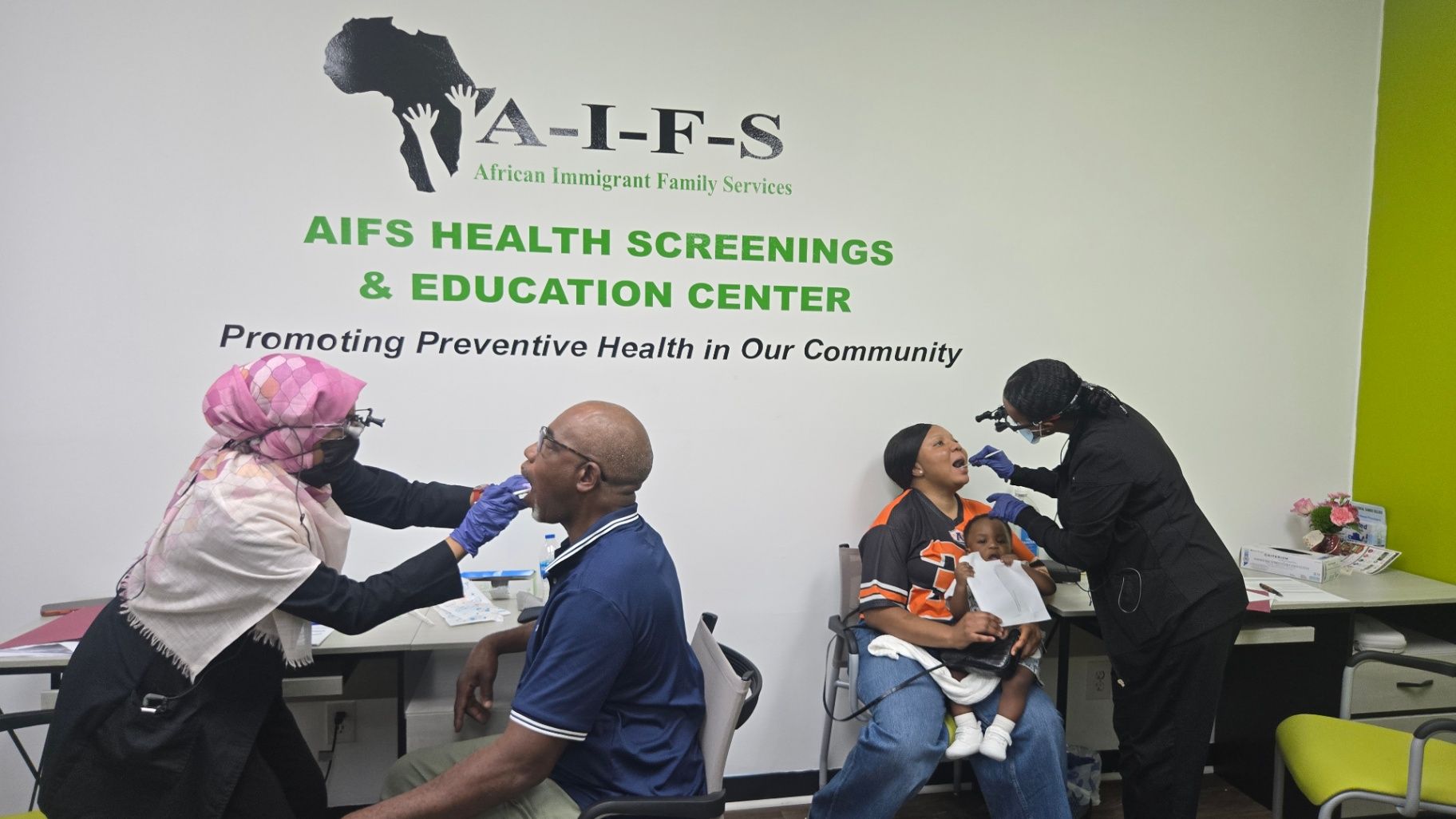 Two screening activities take place at tables, with healthcare workers attending to seated adults in a room with AIFS signage.